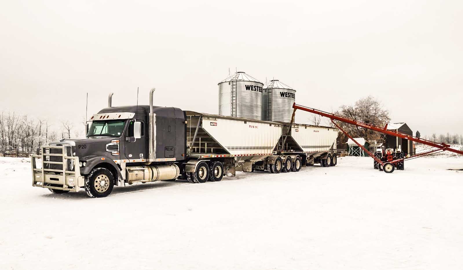 Truck and bulk trailer beside grain bins in winter