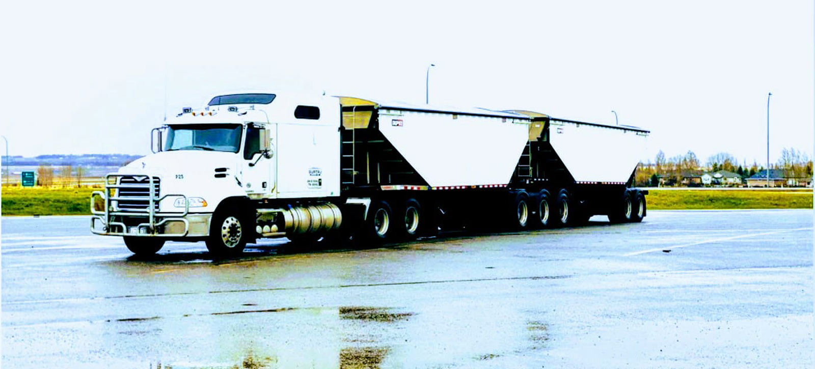 White truck and bulk trailer beside standing water